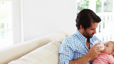 Happy-father-sitting-on-a-sofa-bottle-feeding-to-his-baby