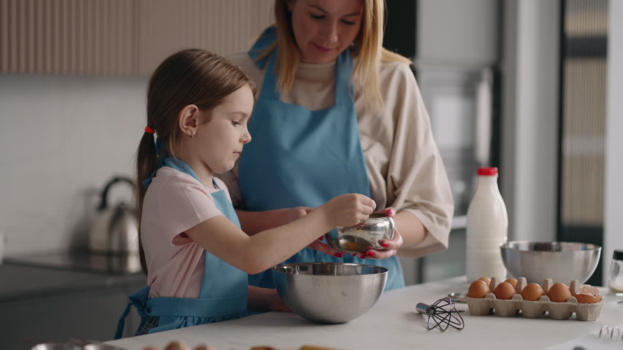 little girl is helping to her mom in kitchen mother and daughter are cooking together adding sugar