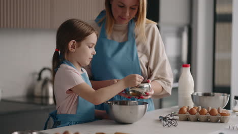 La-Niña-Está-Ayudando-A-Su-Mamá-En-La-Cocina,-La-Madre-Y-La-Hija-Están-Cocinando-Juntas-Agregando-Azúcar