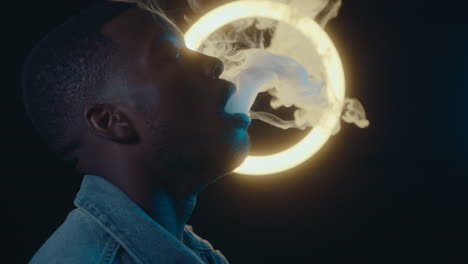 man exhaling vape smoke against ring light