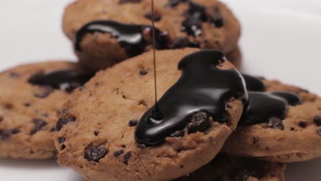 Primer-Plano-Girando-Lentamente-Un-Montón-De-Galletas-Con-Trocitos-De-Chocolate,-Vertiendo-Una-Fina-Corriente-De-Chocolate-Negro-En-Las-Galletas