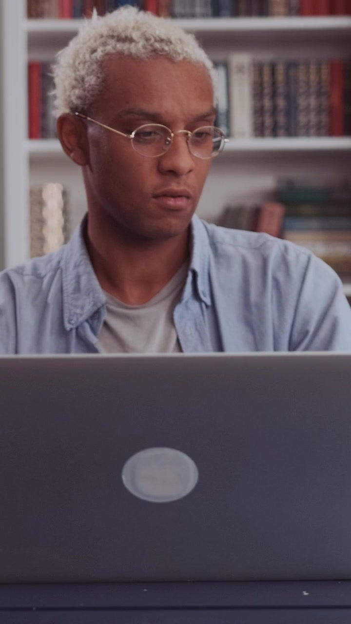 Serious african guy works intently on laptop tilts head slightly with puzzled