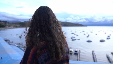 chica mira sobre los barcos en el lago titicaca, vista desde atrás con el pelo soplando en el viento