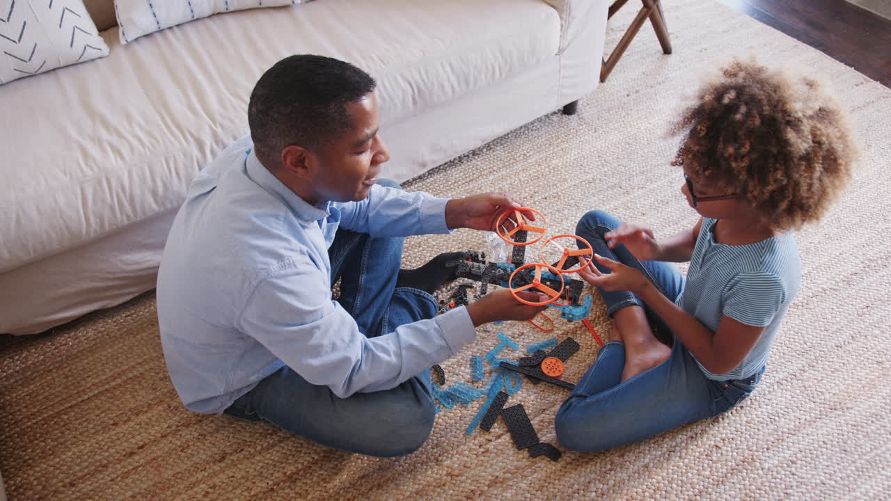 Pre-teen African American girl and grandad sitting cross legged on the floor constructing a toy, elevated view