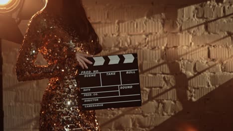 woman in a gold sequin dress holding a clapperboard