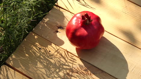 single ripe red pomegranate on wood decking next to grass in sunny garden