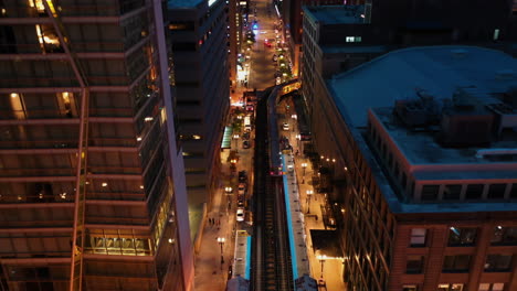 aerial view overlooking a l train driving in middle of buildings in illuminated chicago, usa