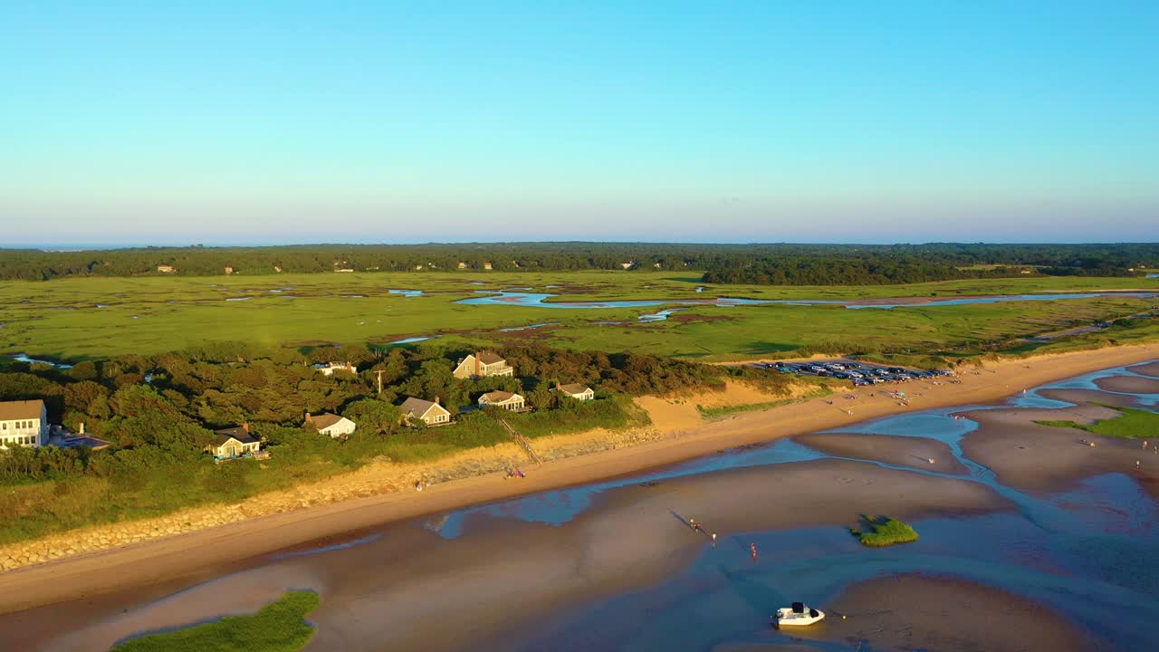 Ripresa aerea da drone di una spiaggia con barriera corallina e una palude nell'entroterra, che mostra tortuosi canali di estuario, ampie piane di marea e un parcheggio sulla spiaggia affollato. Suggestivo panorama sul mare, clip B-roll cinematica fluida in 4K