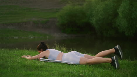 in the morning in the park a woman in sports clothes lying on her stomach raises her arms and legs in turn. exercises for a beautiful body. muscle stabilizers