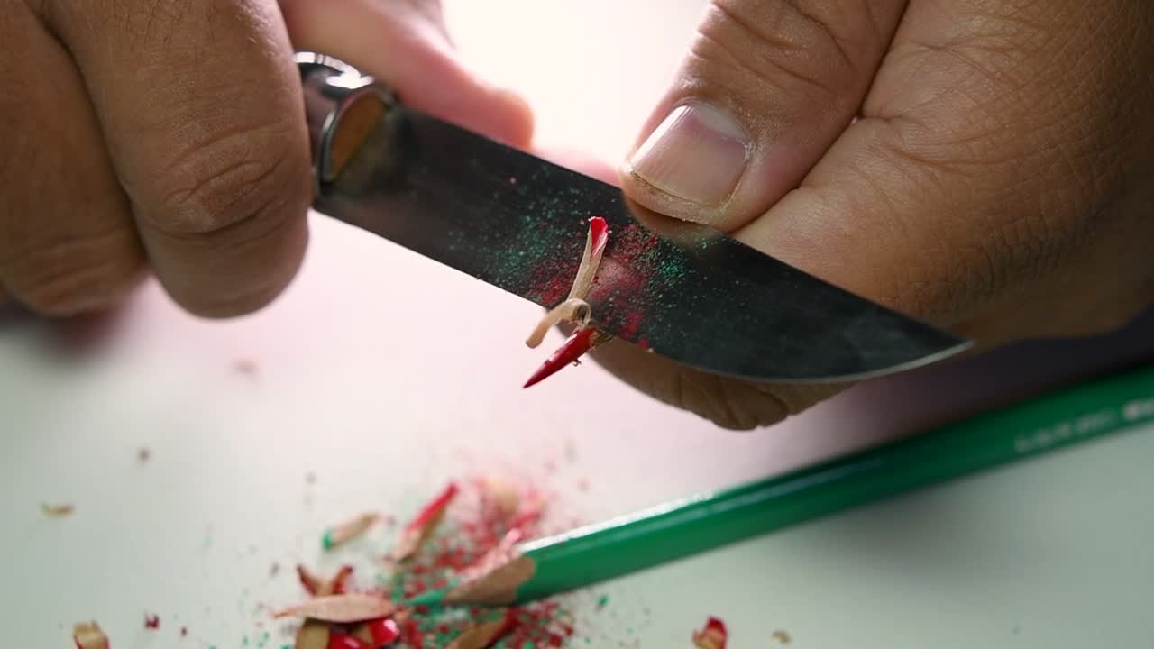 날카로운 칼로 연필과 색연필을 천천히 갈고 있는 손의 영상
