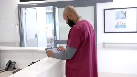 African-american-male-doctor-using-tablet-in-hospital-reception,-slow-motion