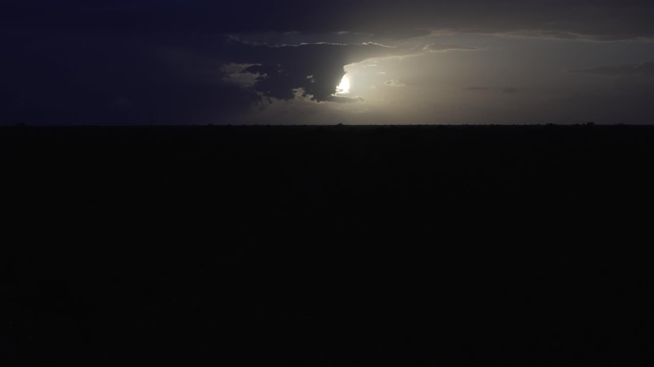Sun or moon in dark sky, illuminating a vast, empty landscape at dusk. Clouds gather ominously, showcasing nature's power in a dramatic display.