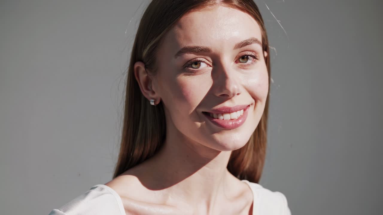 Close-up video frame of a smiling woman in soft lighting, captured from a slightly high angle