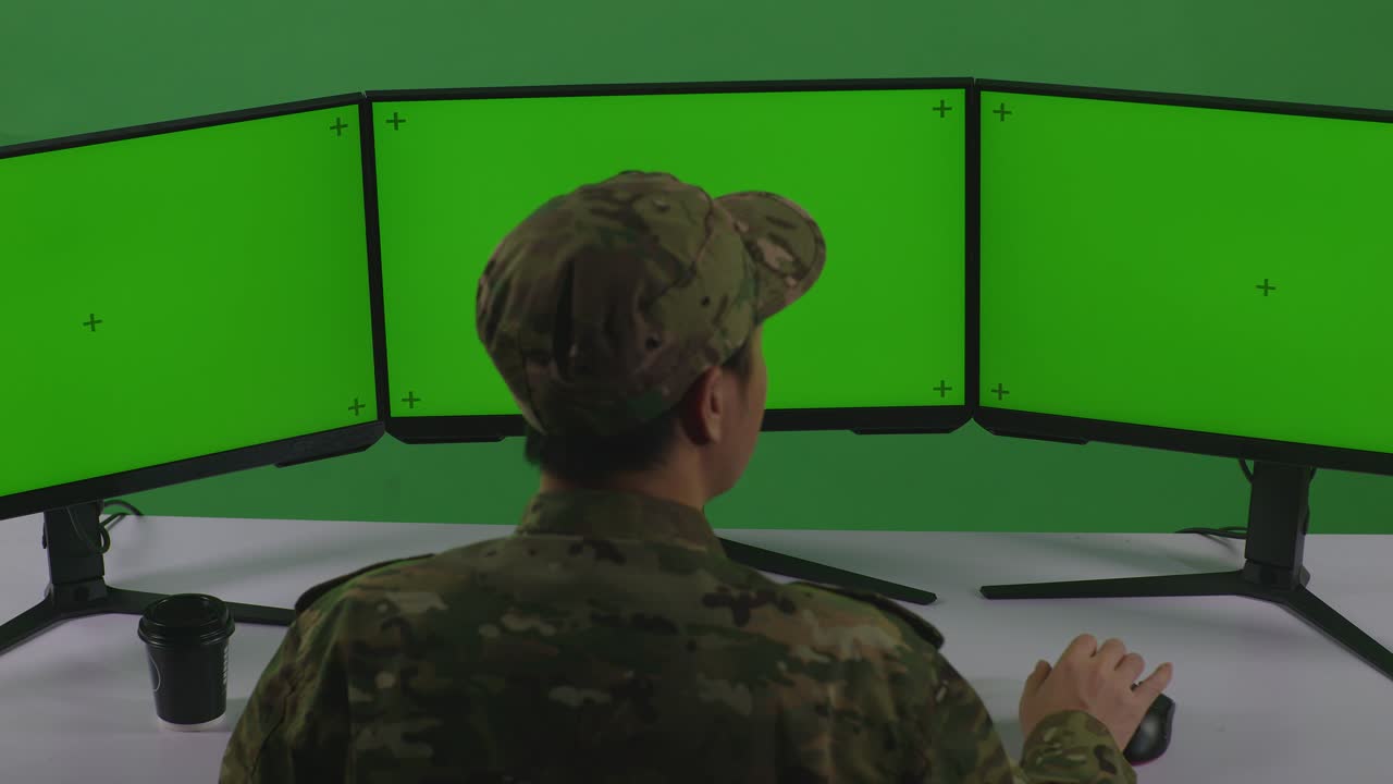 vista trasera de un feliz soldado asiático celebrando y bailando mientras trabaja con un simulacro de varios monitores de computadora en un estudio de pantalla verde