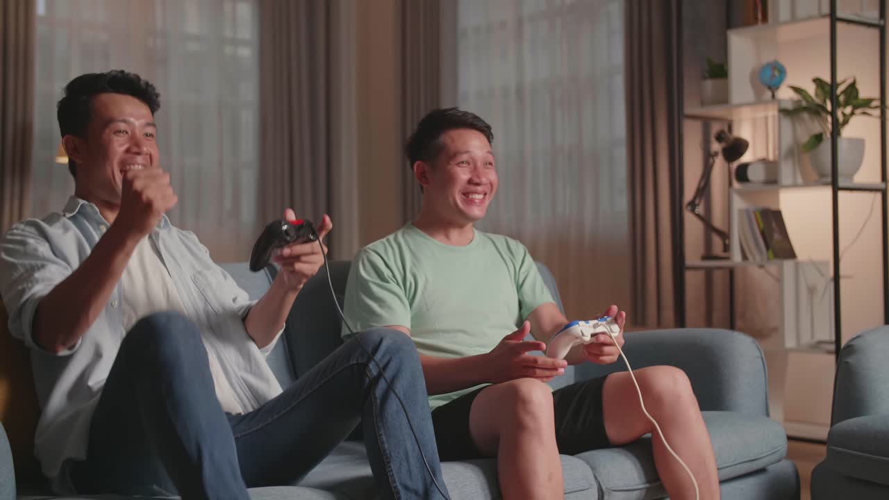 Asian Friends With Joystick Playing Video Games And Celebrating Victory At Home
