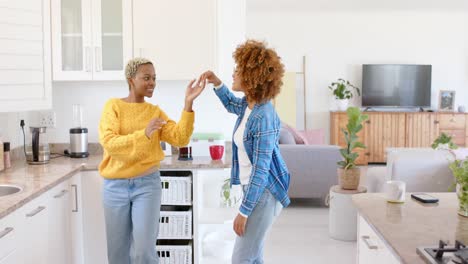 happy diverse female lesbian couple dancing in kitchen in slow motion