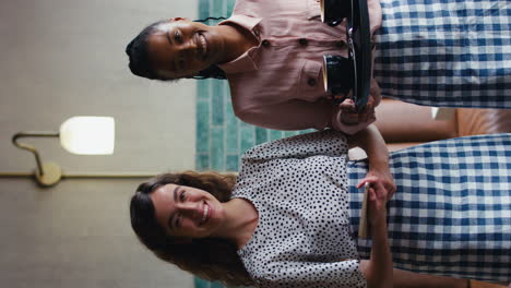 video vertical de dos dueñas sonrientes o personal con tableta digital y tazas en una cafetería