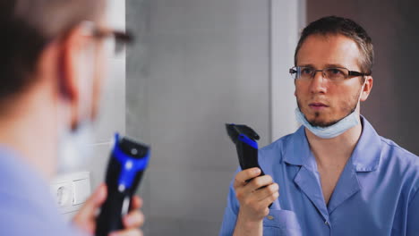 el médico pensativo sostiene un cortador eléctrico cerca de un gran espejo