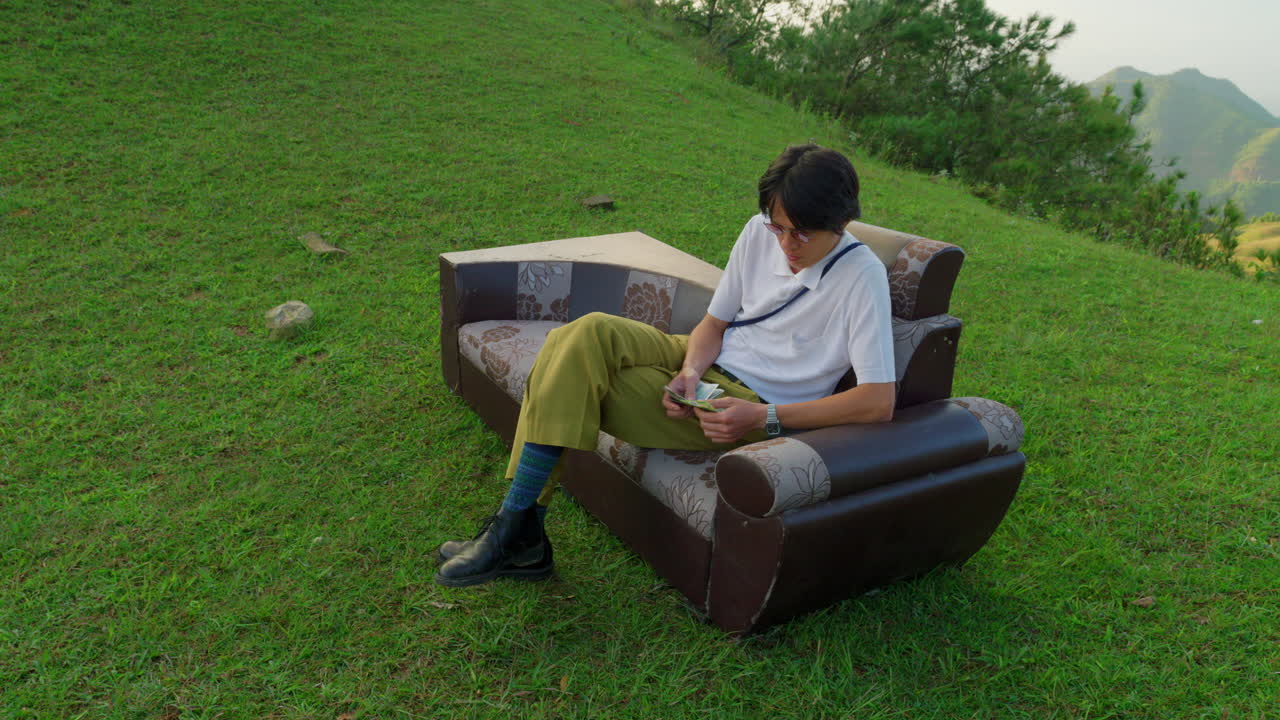 successful businessman sitting outdoor on fancy couch sofa while counting note bills currency money