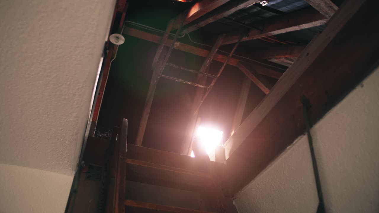 Bottom View of an open vintage roof hatch, seeing the skylight with a sunny lens flare and the timber beams of an old farmhouse