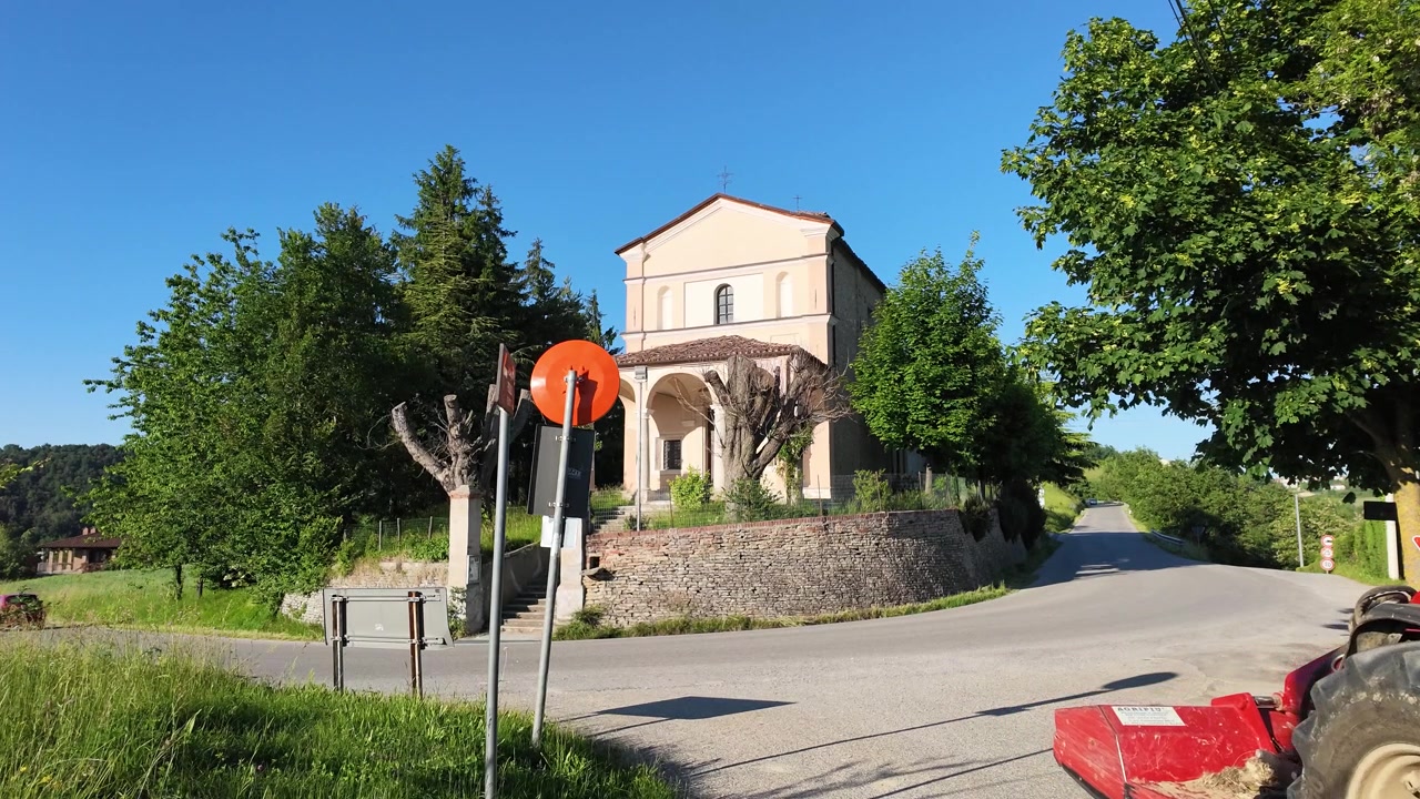 Un trattore rosso percorre una strada di campagna assolata passando accanto a una chiesa tradizionale italiana
