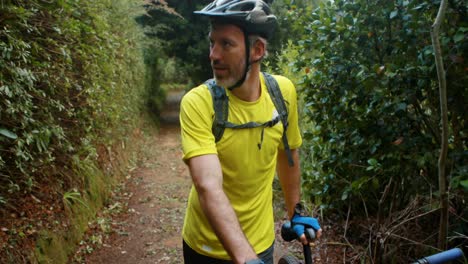 Male-cyclist-walking-with-mountain-bike-in-forest