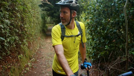 ciclista masculino caminando con bicicleta de montaña en el bosque