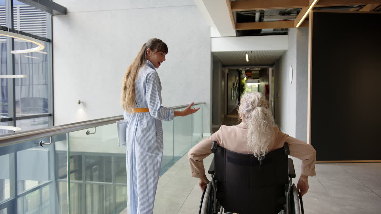 Woman in wheelchair talking with colleague in modern office hallway