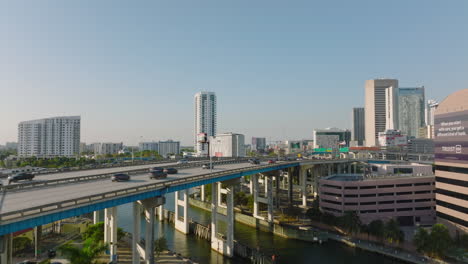 Sliding-reveal-of-traffic-on-highway-bridge-over-river.-Vehicles-driving-on-multilane-trunk-road-in-city.-Miami,-USA