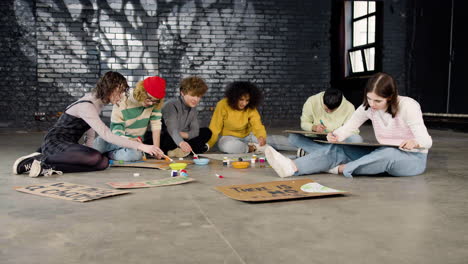 jóvenes activistas ambientales pintando carteles sentados en el suelo
