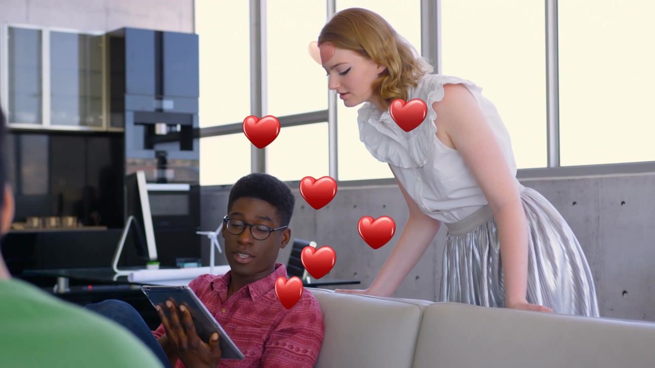 Multiple red heart icons floating over diverse male and female colleagues discussing at office