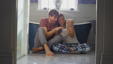 excited couple with woman with prosthetic arm sitting on bathroom floor with positive pregnancy test