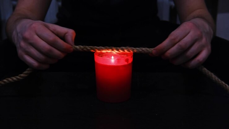 Bruciare una corda di iuta con la fiamma di una candela per il rituale shibari.
