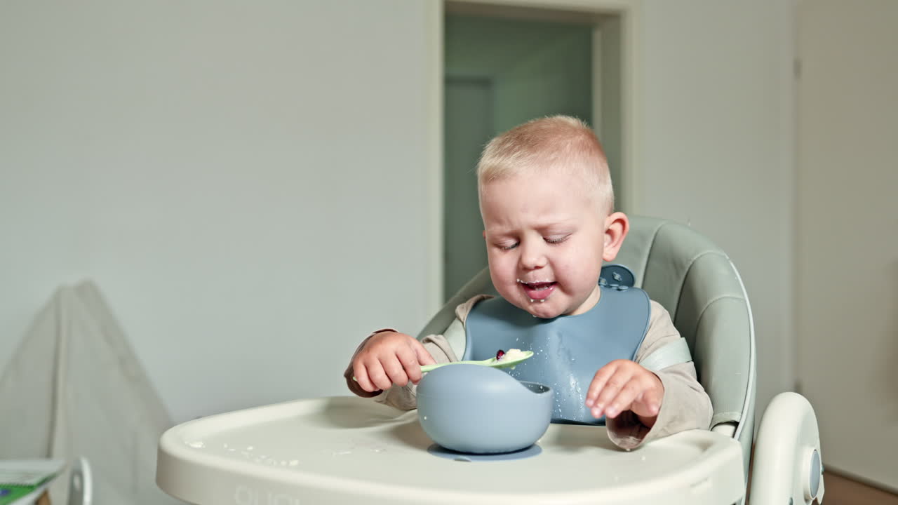 Happy toddler eats with a spoon by himself, child eats milk porridge. Boy 2 years old eats porridge from silicone children's dishes. Healthy baby food. Useful food for children