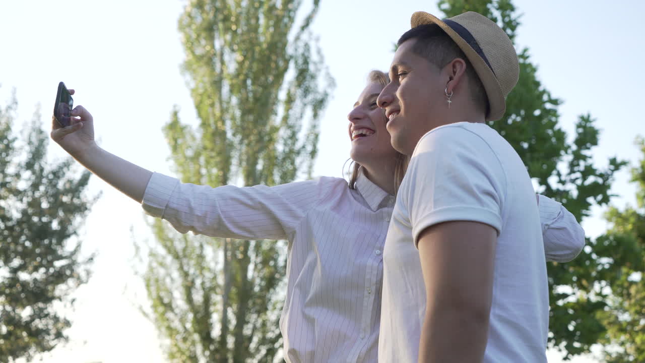 Young couple taking a selfie on their mobile in the park. Latin man and Caucasian woman