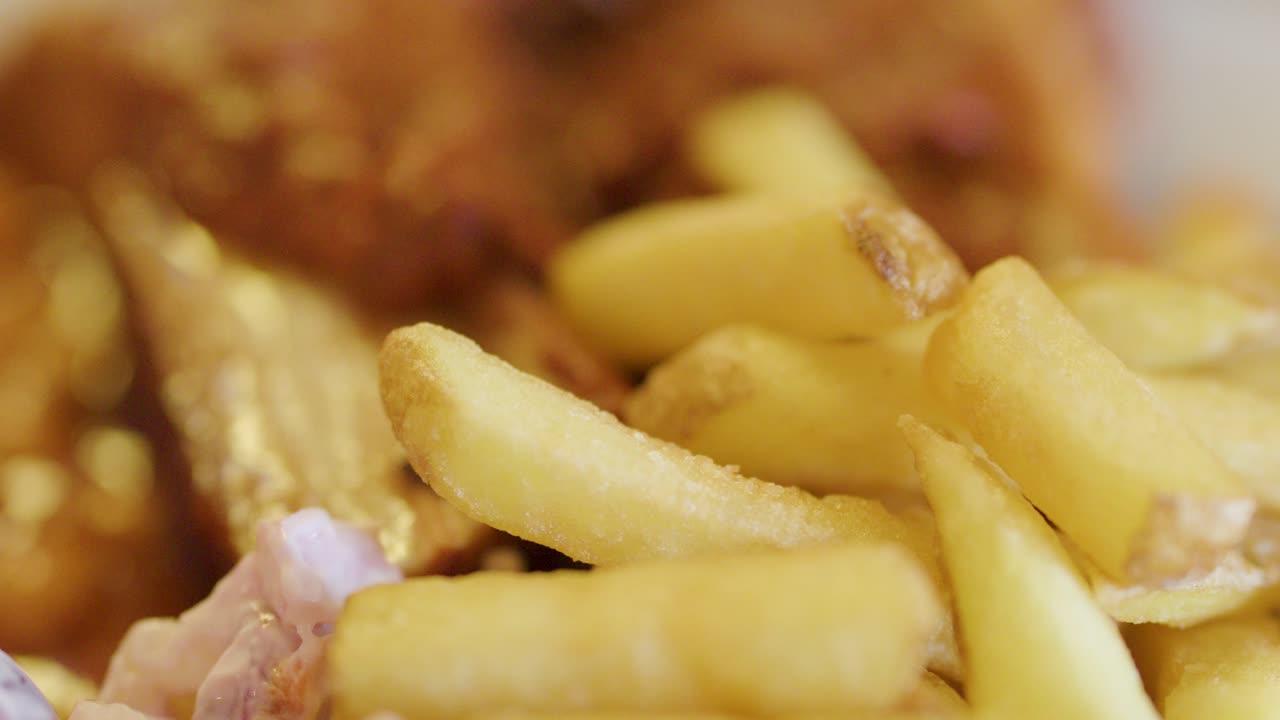 Crispy French fries and battered fish are shown in extreme close-up with shallow depth of field, under warm, natural lighting. Minimal camera movement