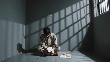 a prisoner in a cell writing in a book