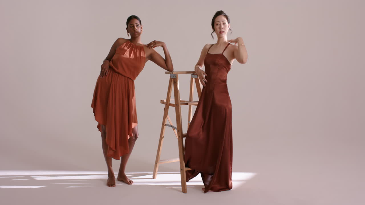 Diverse female models entering studio leaning tilting on stepladder under soft light for shoot