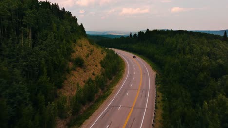 Luftdrohnen-Push-In-Eines-Einsamen-Autos,-Das-Auf-Einer-üppigen-Zweispurigen-Autobahn-Mitten-Im-Nirgendwo-Um-Die-Kurve-Fährt