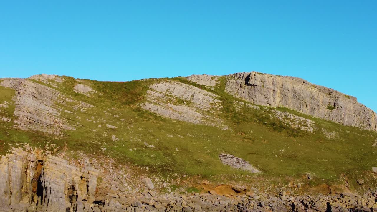 Sideways Aerial Displaying Rocky Terrain of Gower Coast with Clear Blue Sky and Steep Dramatic Cliffs. Beautiful Welsh Countryside. Travel Nature Drone Clip