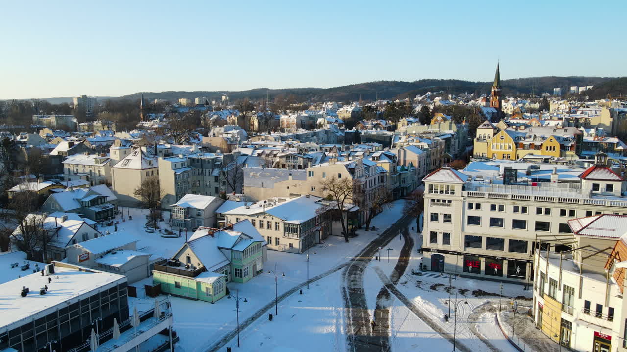hermoso paisaje invernal nevado de la ciudad de sobot con edificios, caminos nevados y colinas en el fondo mientras la luz del sol - vuelo aéreo hacia atrás