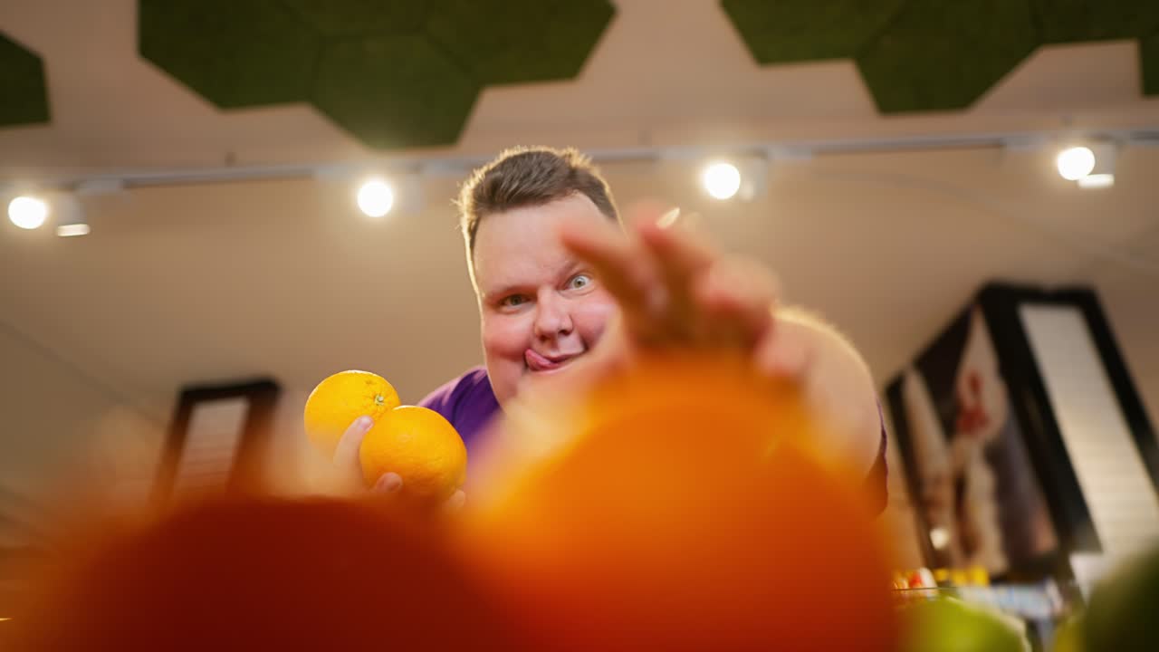 счастливый мужчина с веселой и жаждущей гримасой выбирает апельсины прямо с прилавка. мужчина немного вытягивает язык и берет третий апельсин для себя