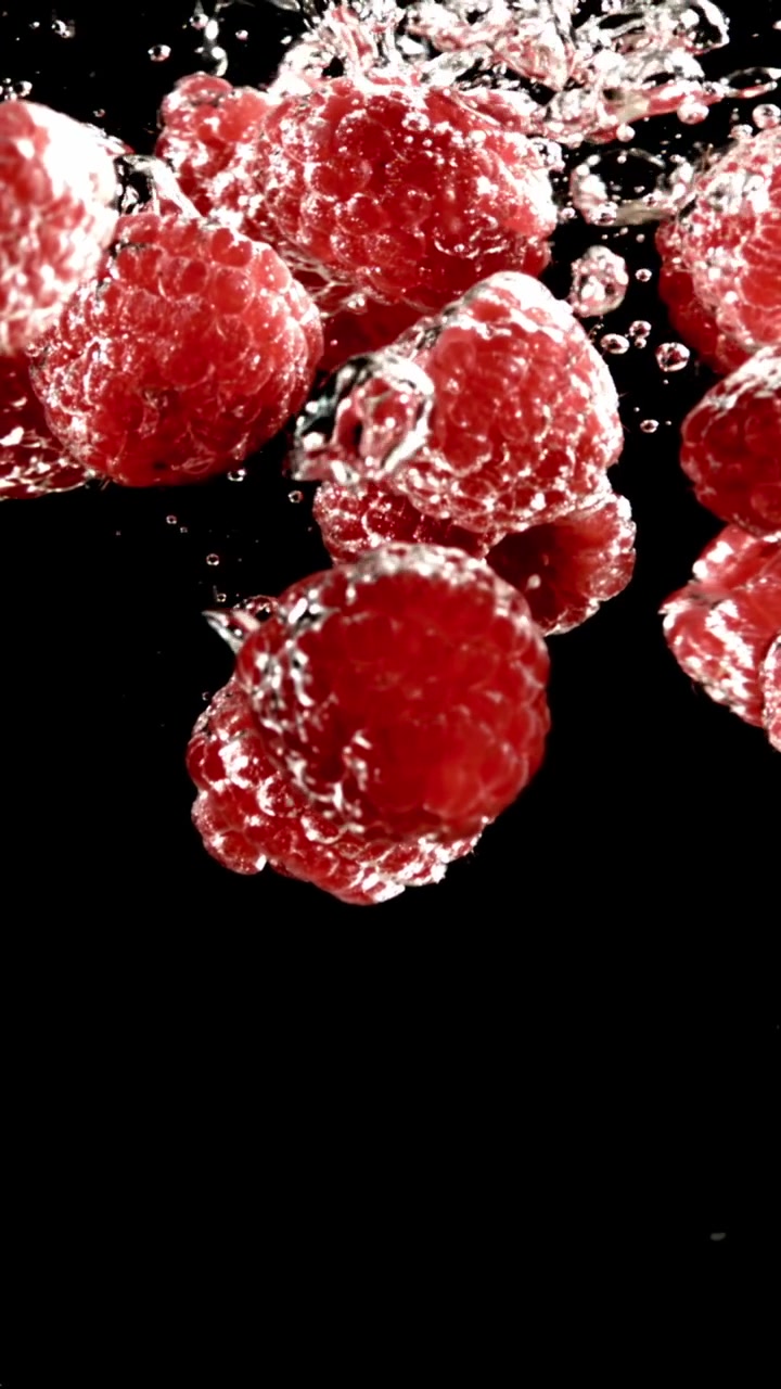 Red Raspberries Falling into Water with Bubbles on Black Background