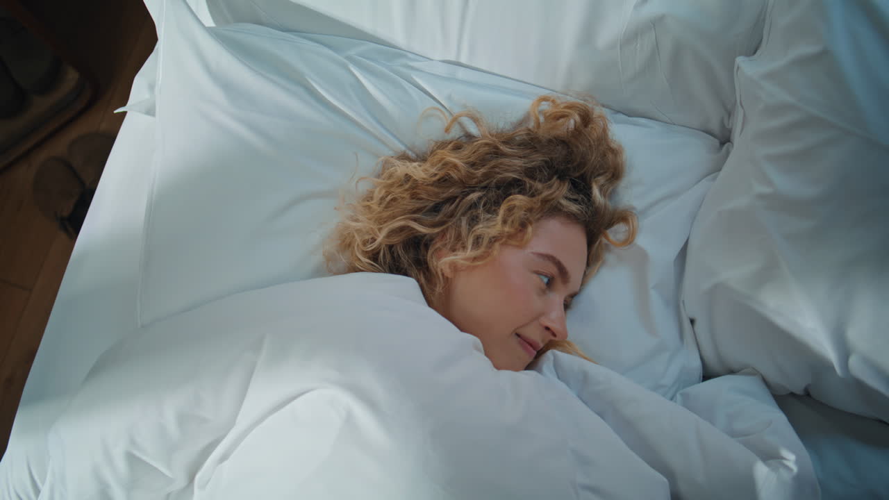Peaceful woman napping bed in morning sunlight. Closeup curly girl waking up