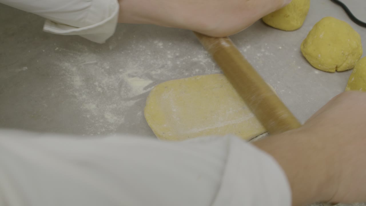 Chef rolls out pasta dough on kitchen cooking table