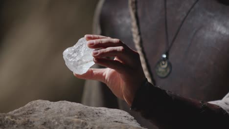 a hand in a leather bracer picks up a large, precious crystal from a rock, inspects it, and stores it in a pouch. fantasy treasure discovery or magic quest concept