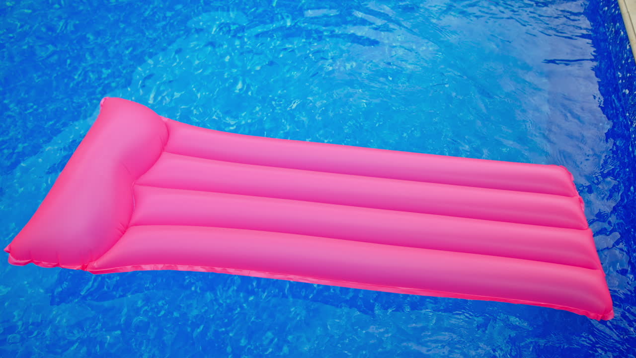 Pink swimming mattress moving by the pink surface of water. Inflatable mattress in the swimming pool. Top view.
