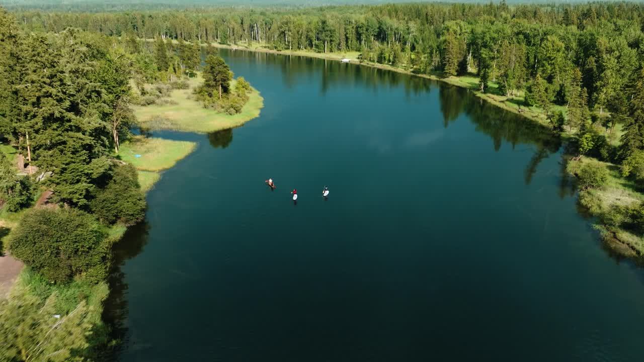 Aerial drone pull away of family of 3 stand up paddle boarding on pristine river with lush green shorelines and mountains in the background