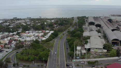 Aerial-forward-tilt-up-reveal-over-Nunez-de-Caceres-road-in-Santo-Domingo-and-ocean-in-background