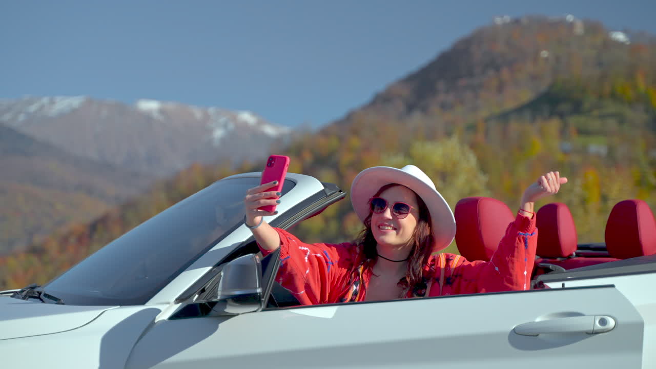 mujer tomando una selfie en un coche descapotable en las montañas durante la caída